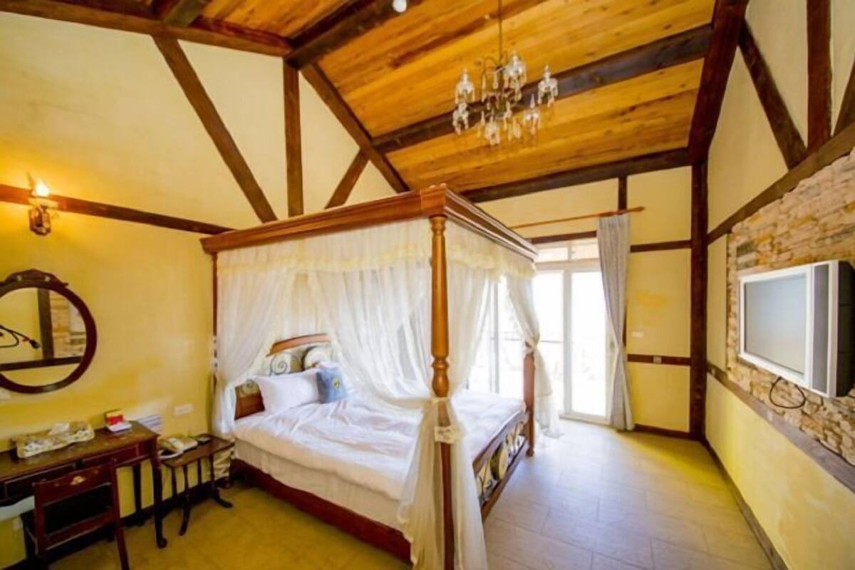Un dormitorio con cama con dosel, un escritorio de madera, un espejo y una araña.
