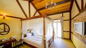 A bedroom with a four-poster bed, a wooden desk, a mirror, and a chandelier.