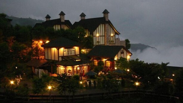A large, multi-story building with a prominent tower, surrounded by lush greenery and a misty backdrop. - Xiangqing Garden Leisure Cabin (Nantou)