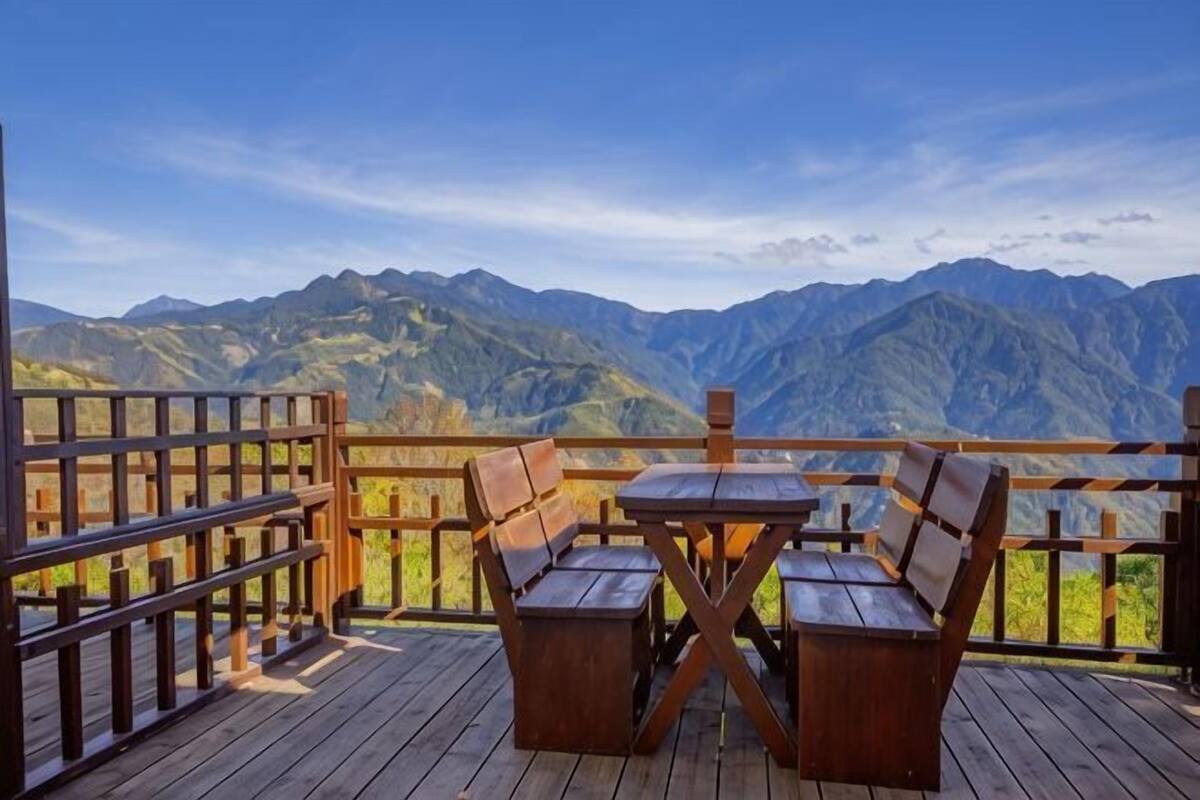 Una terraza de madera con una mesa y sillas, con vistas a un paisaje montañoso.