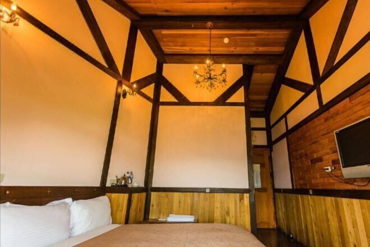 Una habitación con cama, vigas de madera, candelabro y televisión en la pared.