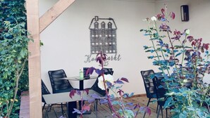 Un espacio de patio cubierto con mesa y sillas, un mural en la pared y plantas trepadoras.