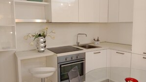 A modern kitchen with white cabinetry, a stainless steel sink, an oven, and a glass dining table. - Holiday Home Near Pizzo Beach (Pizzo)
