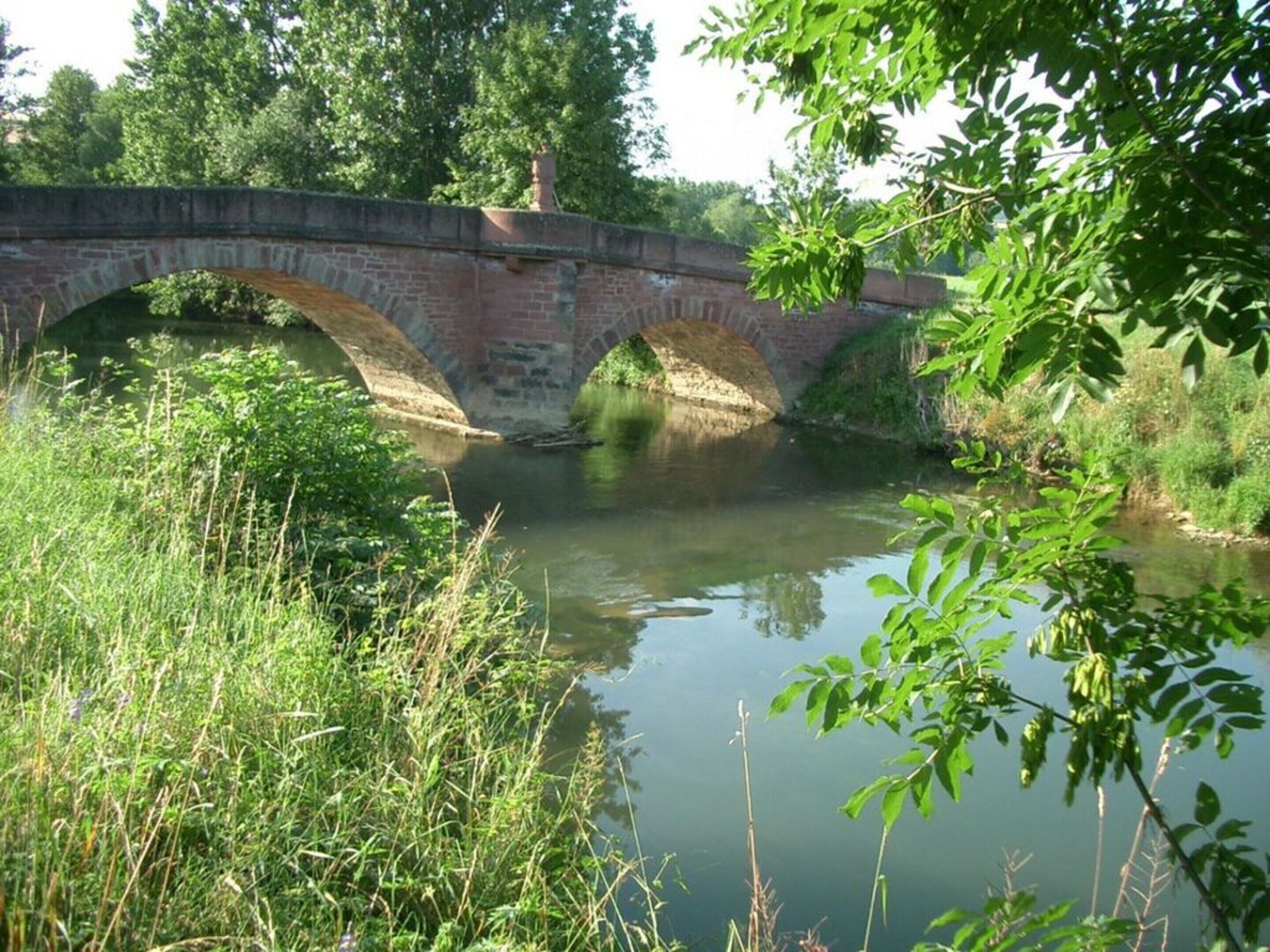 A stone bridge over a calm river with lush greenery around.