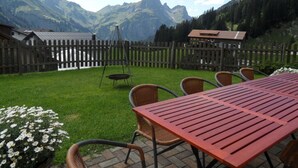 A patio with a red table and wicker chairs, surrounded by a wooden fence, with a mountain view in the background. - Amazing Apartment in Schrocken (Schroecken)