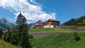 Un bâtiment moderne doté d’un toit en pente, entouré d’une végétation luxuriante et avec des montagnes en arrière-plan.
