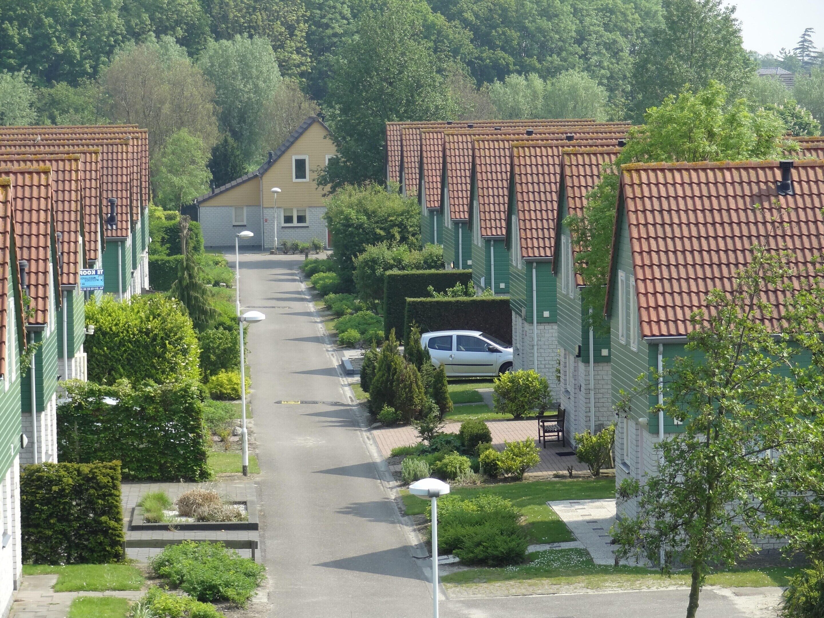 Reihenhäuser mit roten Ziegeldächern, eine zentrale Straße und Grünflächen.