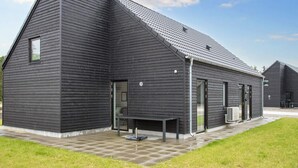 Un bâtiment moderne doté d’un toit en pente, de grandes fenêtres et d’une terrasse dallée.