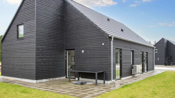 Un bâtiment moderne doté d’un toit en pente, de grandes fenêtres et d’une terrasse dallée.