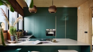 A modern kitchen with a central island, two bar stools, a built-in oven, and a hanging light fixture. - Apartment in Drenthe Near National Park (Appelscha)