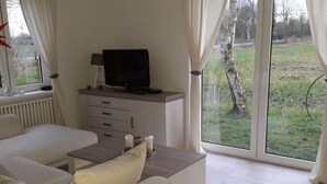 A modern living room with a sofa, a coffee table, a flat-screen TV on a wooden stand, and a sliding glass door leading to a garden. - Country House Country Idyll With Garden (Norden)
