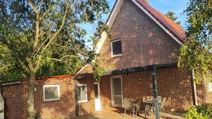 A two-story brick house with a red-tiled roof, a covered patio with outdoor furniture, and a small garden area. - Country House Country Idyll With Garden (Norden)