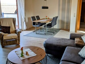 A modern living room with a sofa, a round coffee table, and a dining area with a table and chairs. - Holiday Apartment Moorwiese (Hoerstel)