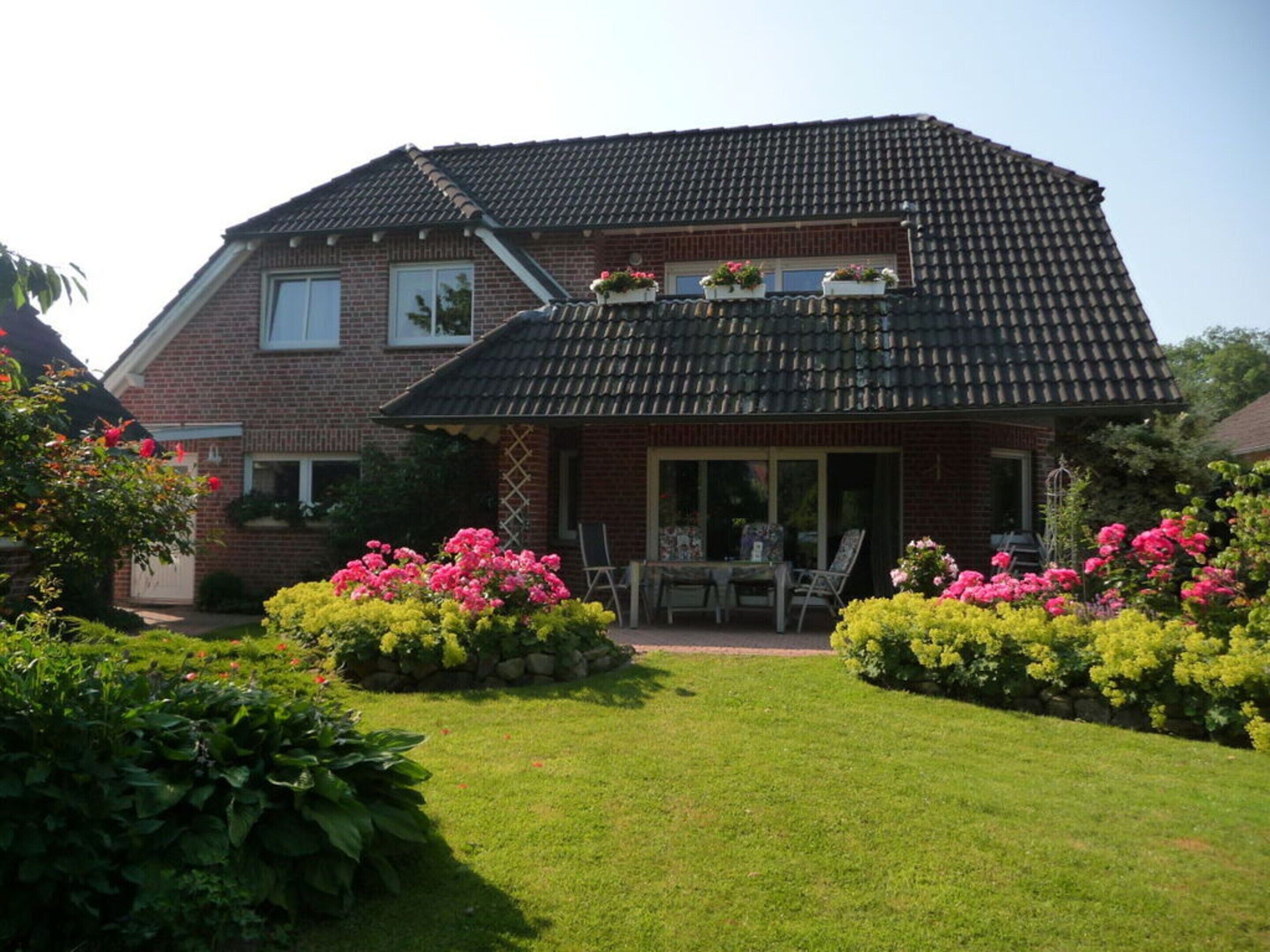 A two-story brick house with a tiled roof, a covered patio with outdoor furniture, and a well-maintained garden with flowering plants.