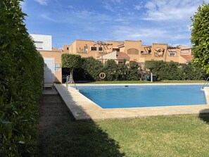 A swimming pool with a clear blue water, surrounded by a well-maintained lawn and hedges. In the background, there are buildings with a uniform architectural style, featuring flat roofs and beige walls. - Belvilla by OYO Alameda de Roquetas (Roquetas de Mar)