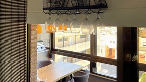 A restaurant interior with a 'BAR' sign, a wooden table, a cushioned chair, and a window with a view of buildings.
