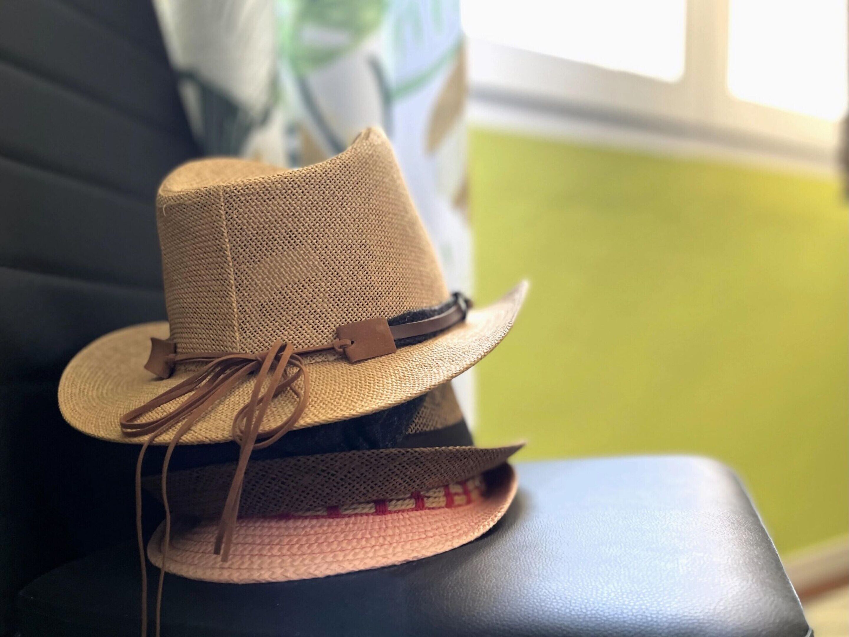 A straw hat with a brown band and tassel on a black leather chair.