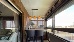 A modern living room with a sofa, a coffee table, and a dining area with two chairs. There is a large window providing a view of the city.