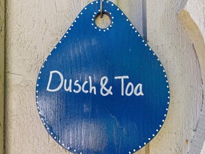 A blue sign with the text "Dusch & Toa" on a wooden surface.