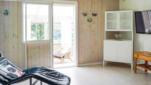 A room with a sliding glass door leading to a balcony, a cushioned bench, a white cabinet with glass doors, and a small table. - 10 Person Holiday Home in Brastad-by Traum (Brastad)