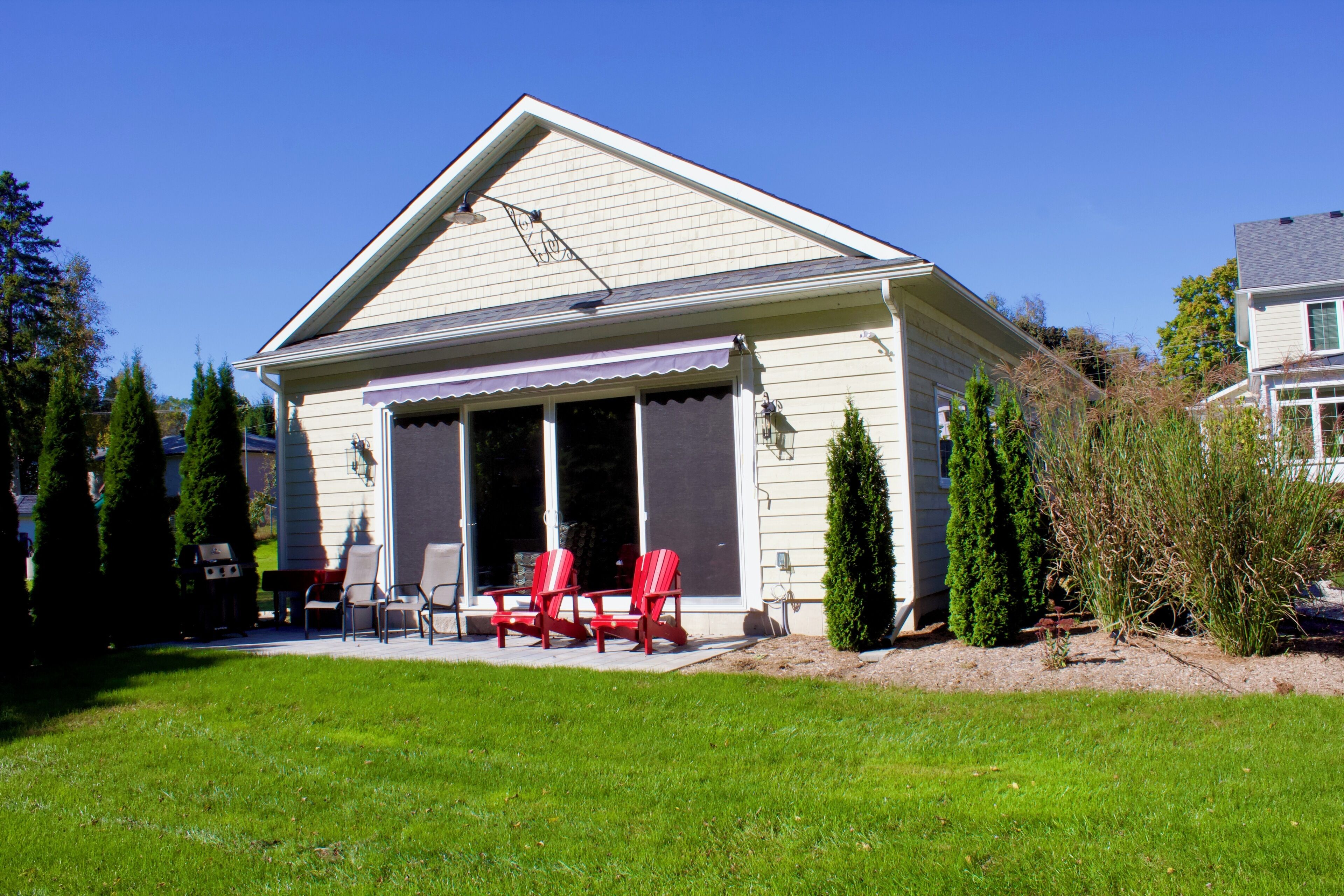 A single-story house with a covered patio area, a barbecue grill, and red Adirondack chairs.