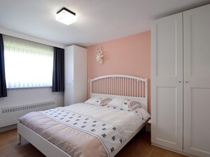 Un dormitorio con cama, radiador, armario y ventana con cortinas.
