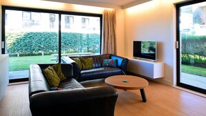 A modern living room with a leather sofa, a round coffee table, and a flat-screen TV. - Sandpiper Apartment With two Rooms (De Haan)