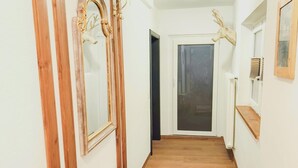 Un couloir étroit avec un plancher en bois, un banc et une porte au fond.