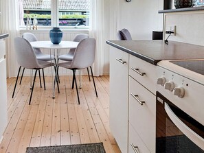 A modern kitchen with a dining table and chairs, a stove, and a view of the outside through a window.