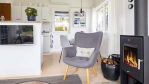 A modern living room with a grey armchair, a glass coffee table, a fireplace, and a kitchen area in the background. - Tranquil Retreat on Eno - By Traum Ferienwohnungen (Karrebæksminde)