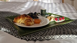 Una cama bien hecha con una bandeja verde que contiene croissants, bayas y una taza de té.