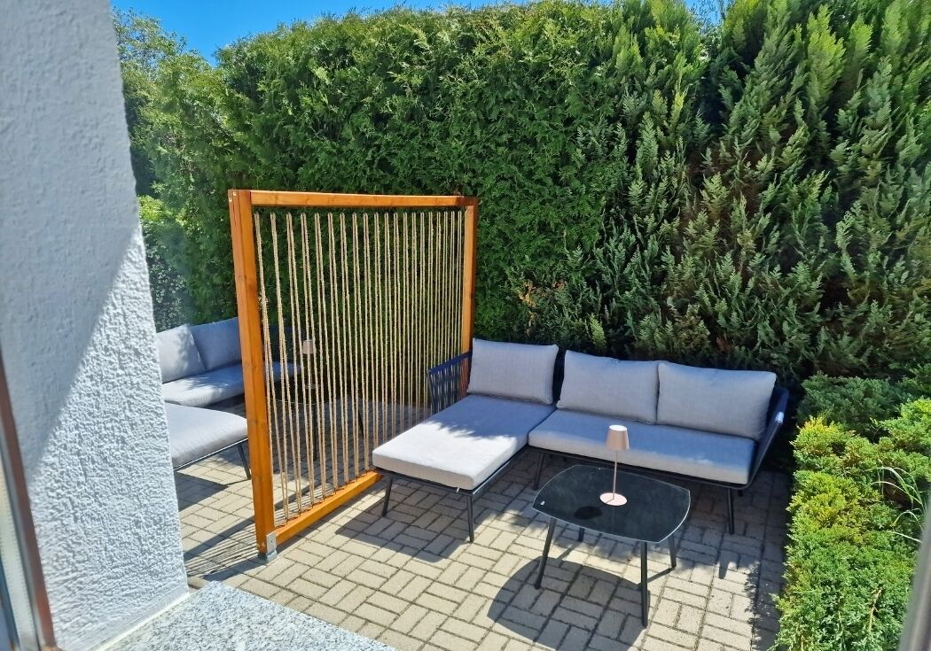 A patio with a wooden fence, a grey sofa, and a small table.
