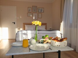 Una mesa de desayuno bien dispuesta con platos, una jarra de jugo de naranja, un florero de flores y una cesta de pan y queso.