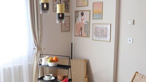 Una sala de estar moderna con un tapete redondo tejido, una mesa de centro de vidrio, un sillón de mimbre y una mesita auxiliar de tres niveles con frutas y una tetera.