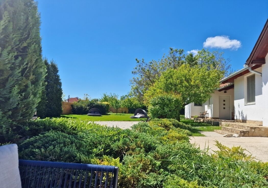 Ein Garten mit Grillplatz, ein weißes Gebäude mit rotem Dach und ein klarer, blauer Himmel.