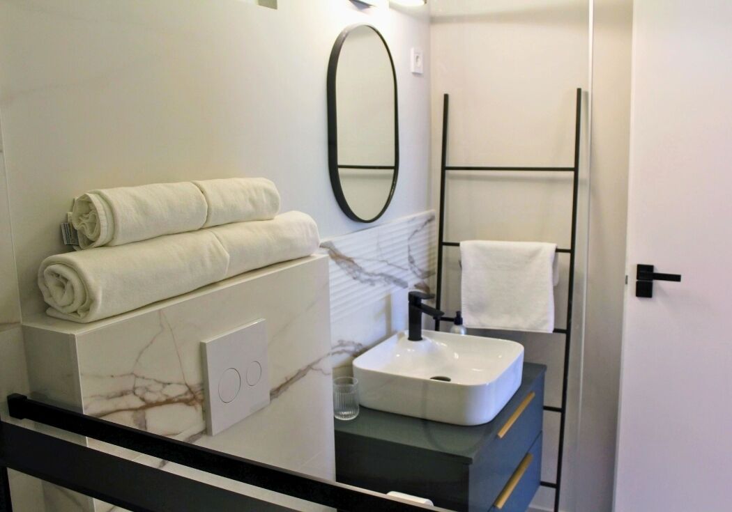 A modern bathroom with a marble vanity, a white sink, a towel rack, and a mirror.