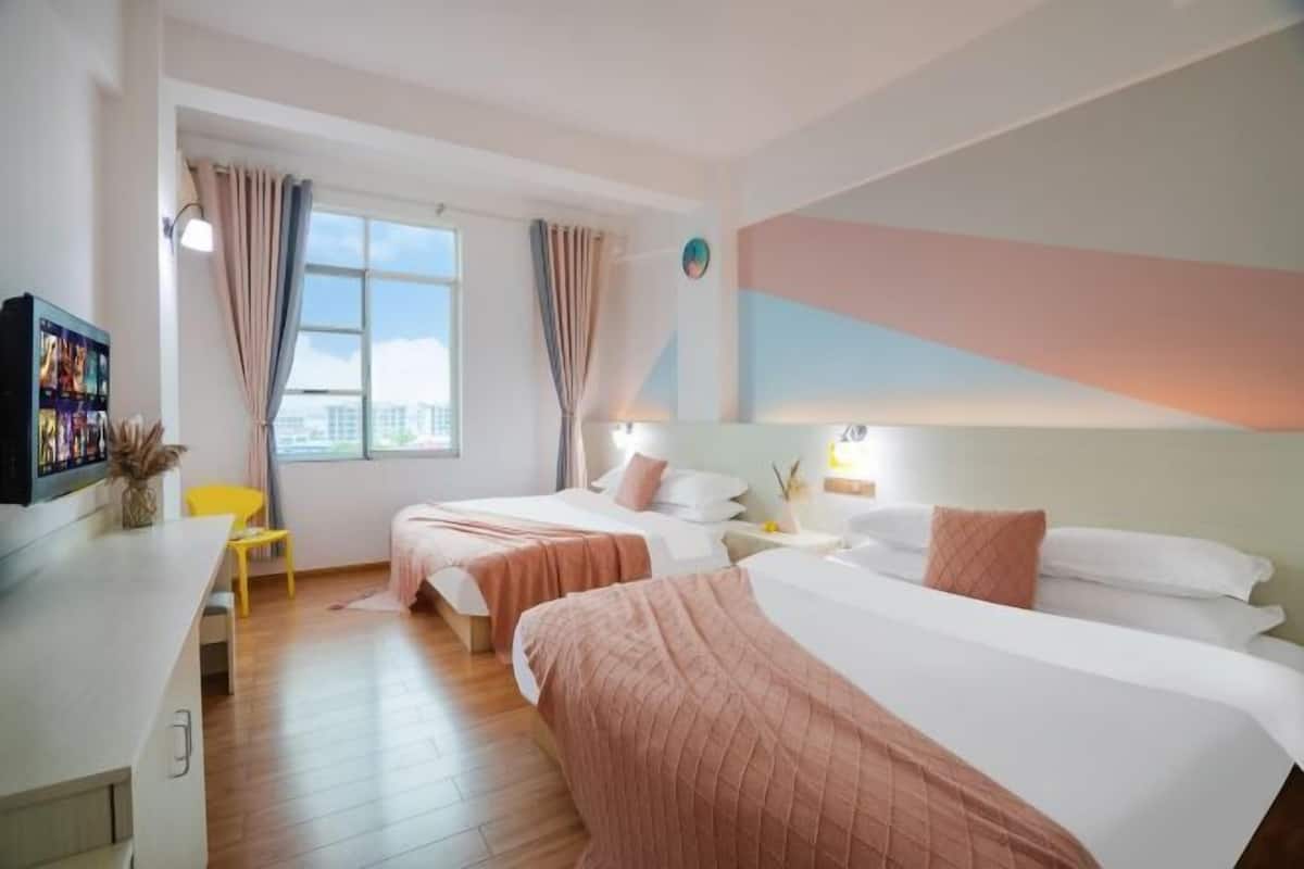 Habitación de hotel con dos camas, un escritorio, una silla y una ventana con cortinas.