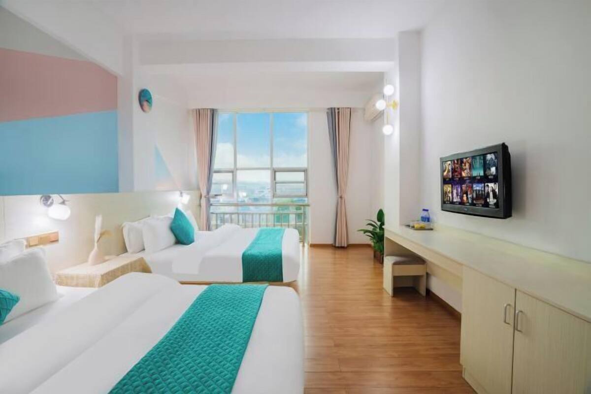 Habitación de hotel con dos camas, televisión, balcón y vistas a la ciudad.