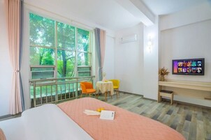 Habitación de hotel con cama, escritorio, televisión, ventana con vista a árboles y dos sillas.