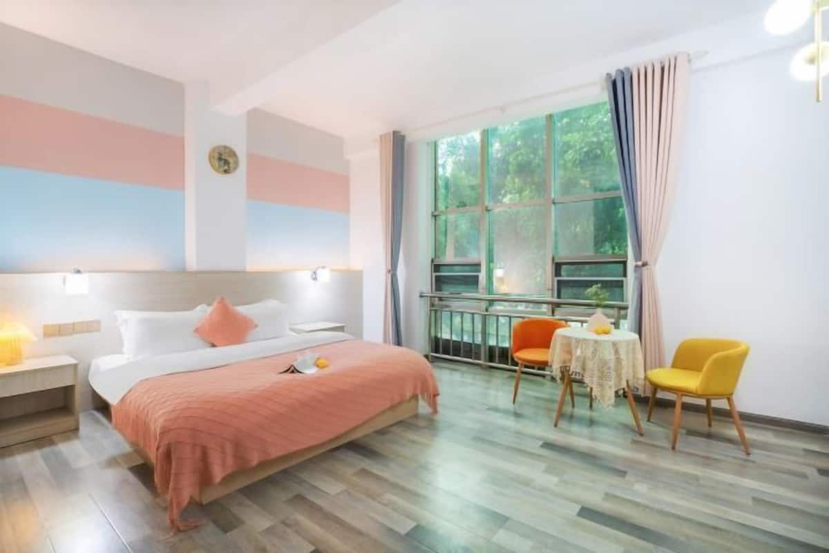 Una habitación de hotel con cama, mesita de noche, ventana con cortinas y una pequeña mesa con sillas.