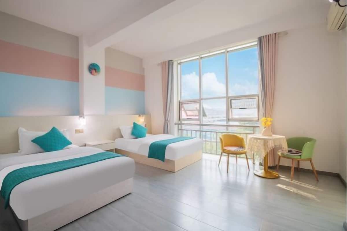 Habitación de hotel con dos camas, un balcón con vistas, una pequeña mesa con un jarrón y una silla.