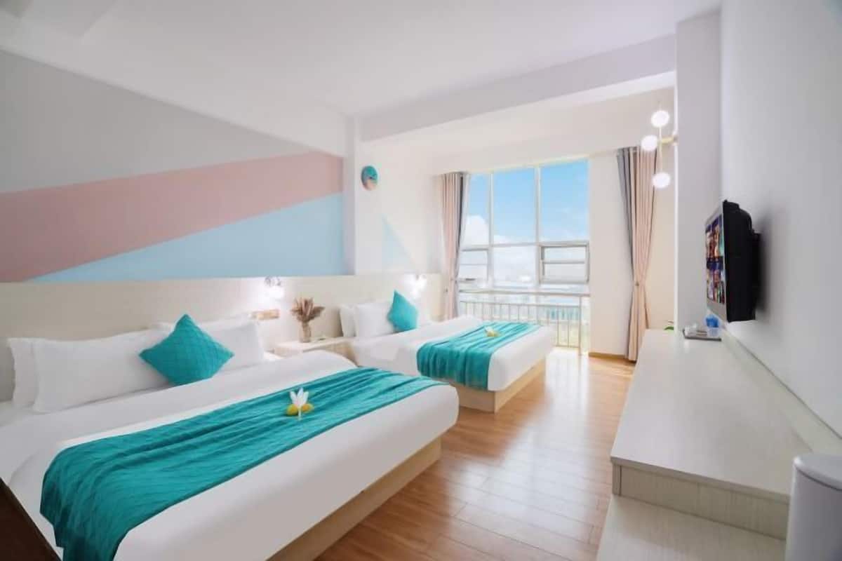 Habitación de hotel con dos camas, televisión, escritorio y balcón con vistas.