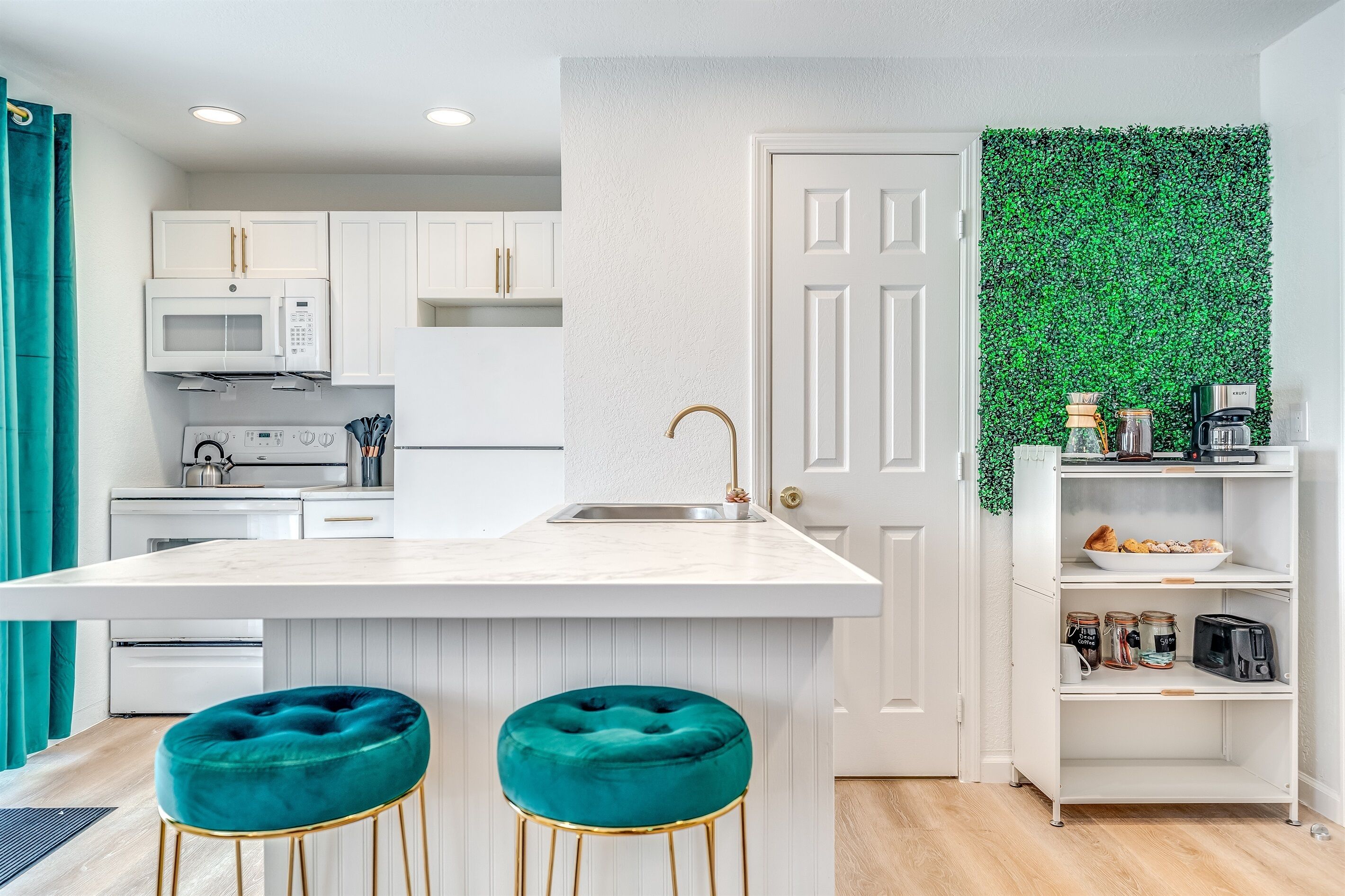 Una cucina moderna con mobili bianchi, un'isola centrale con sgabelli, un forno a microonde, un lavello e una parete verde.