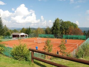 A tennis court with a wooden fence, a covered seating area, and trees in the background. - Mitterdorf Modern Retreat (Philippsreut)