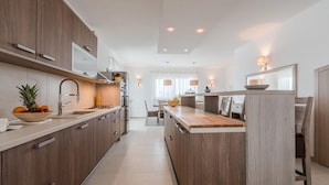 A modern kitchen with wooden cabinets, a central island, and a dining area with a table and chairs. - Apartment in Croatia Near Adriatic Coast (Sukosan)