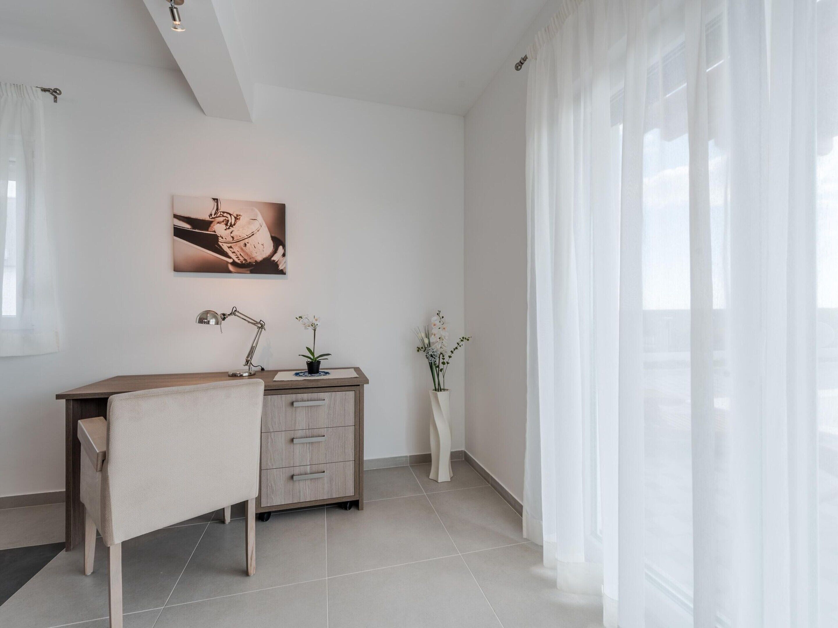 A minimalist office space with a desk, chair, and two potted plants.