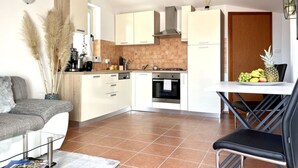 A modern kitchen with white cabinets, a stove, and a dining area with a table and chairs. - Appartement Lady Daniela (Lovran)
