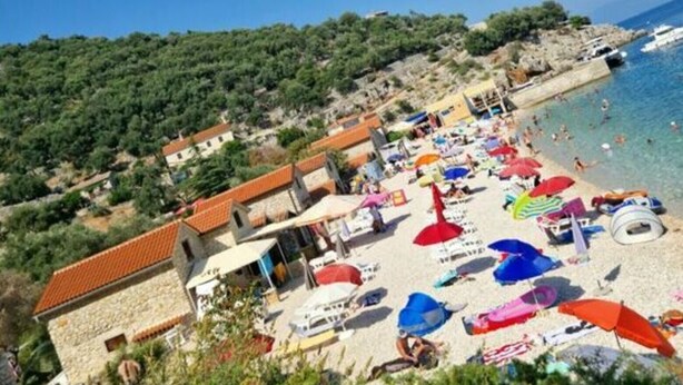 A beach with numerous colorful umbrellas and a few people. There are buildings with red roofs and a rocky hillside in the background. - Appartement Lady Daniela (Lovran)