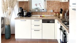 A modern kitchen with white cabinets, a window with blinds, a coffee maker, a toaster, and a dishwasher. - Appartement Lady Daniela (Lovran)