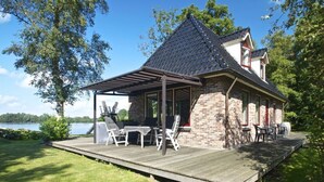 Ett hus med en täckt uteplats, utomhusmöbler och utsikt över en sjö.